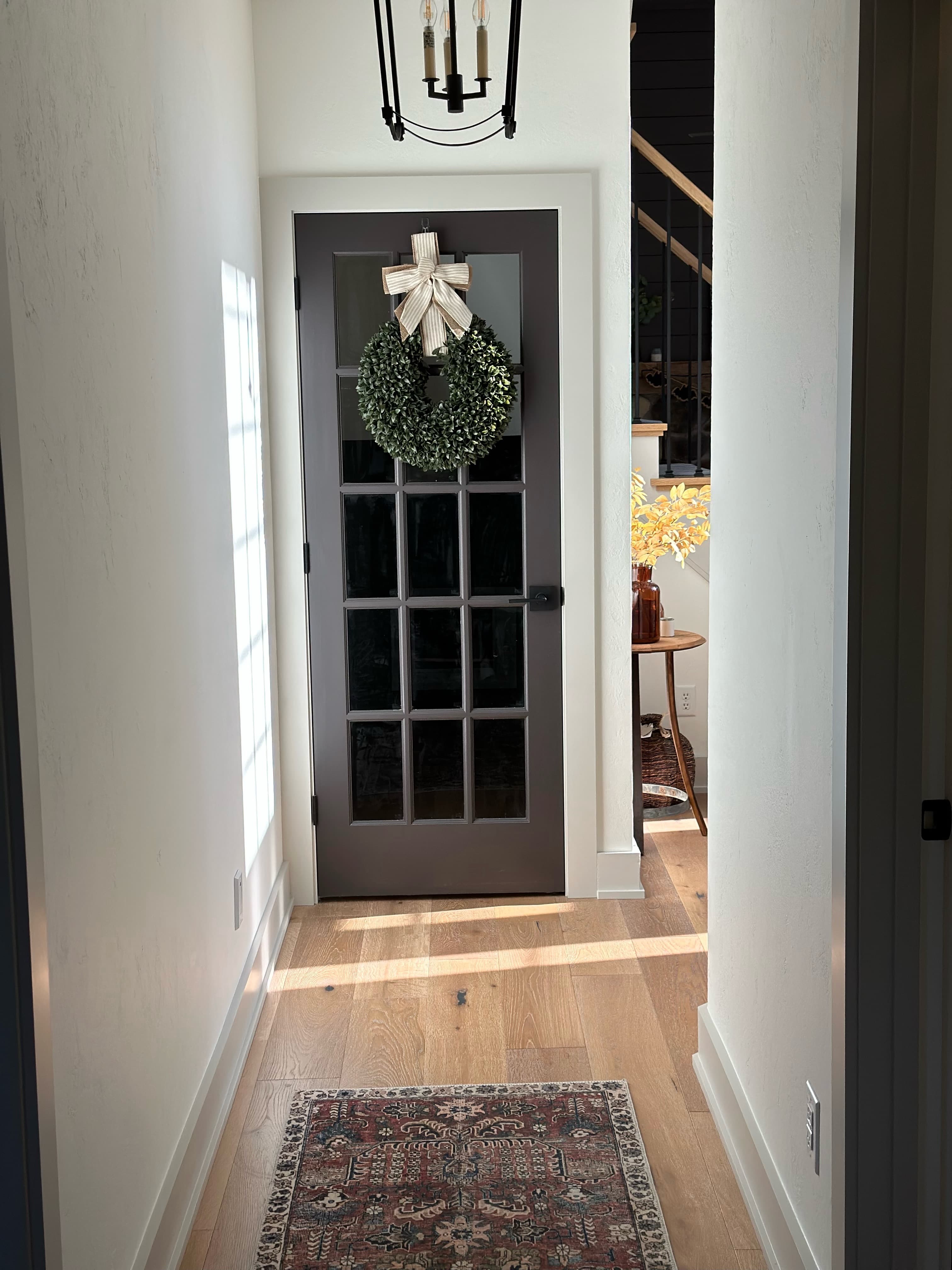 Gray French door with green wreath and striped bow in bright entryway