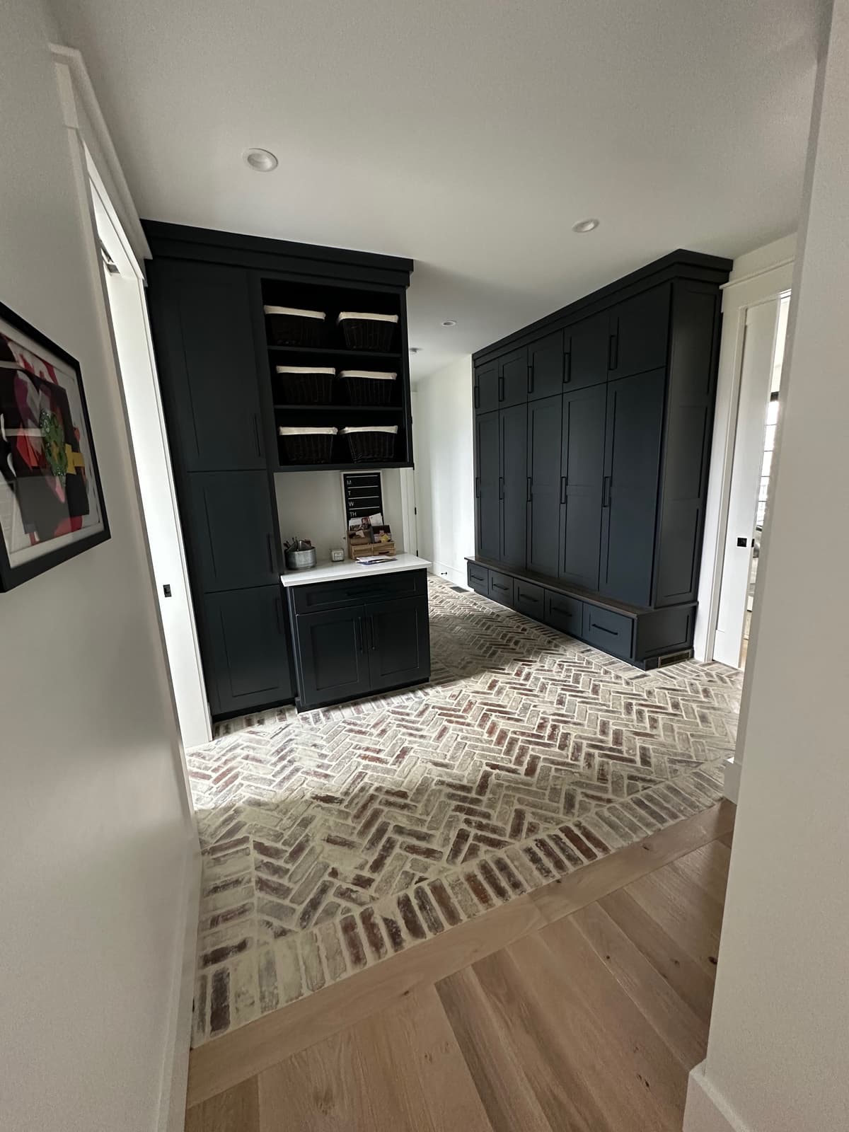 Mudroom with dark gray built-in cabinets and herringbone brick floor