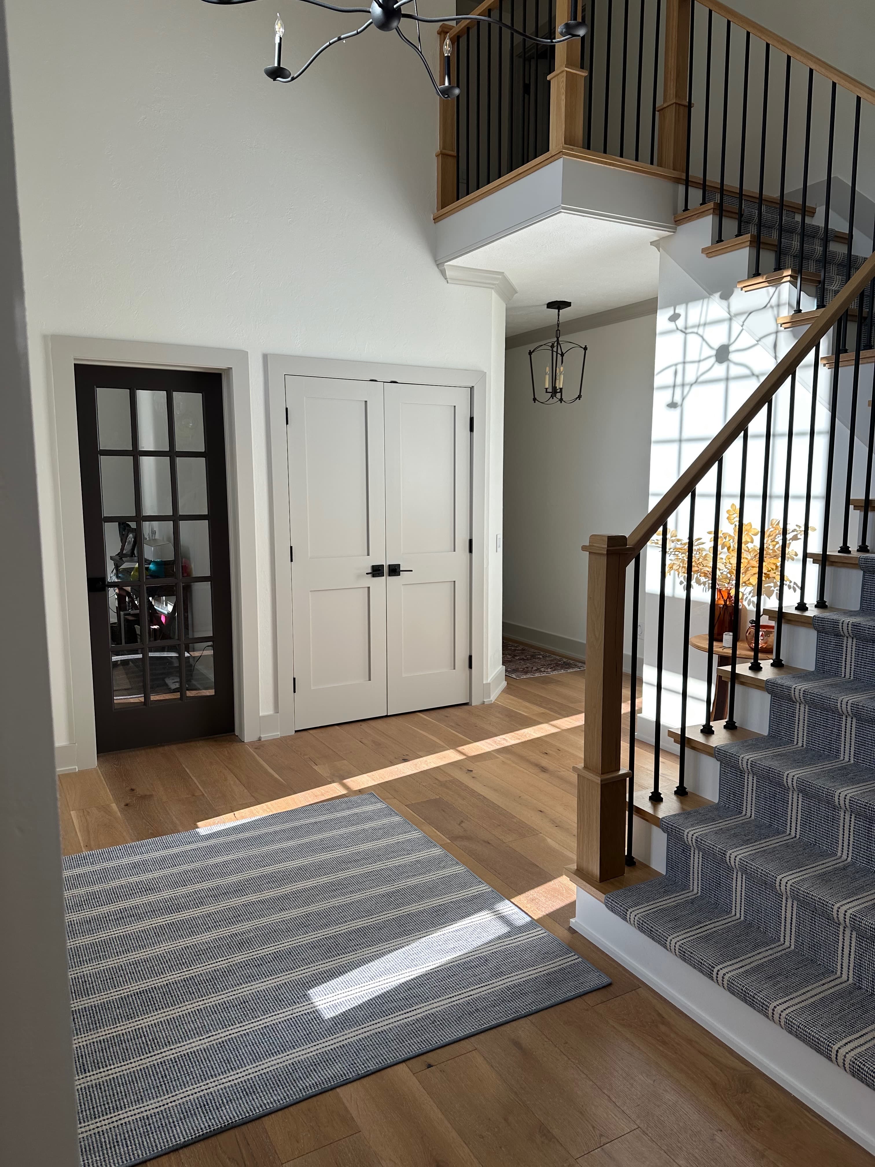 Two-story foyer with wood staircase, striped carpet runner, and white walls