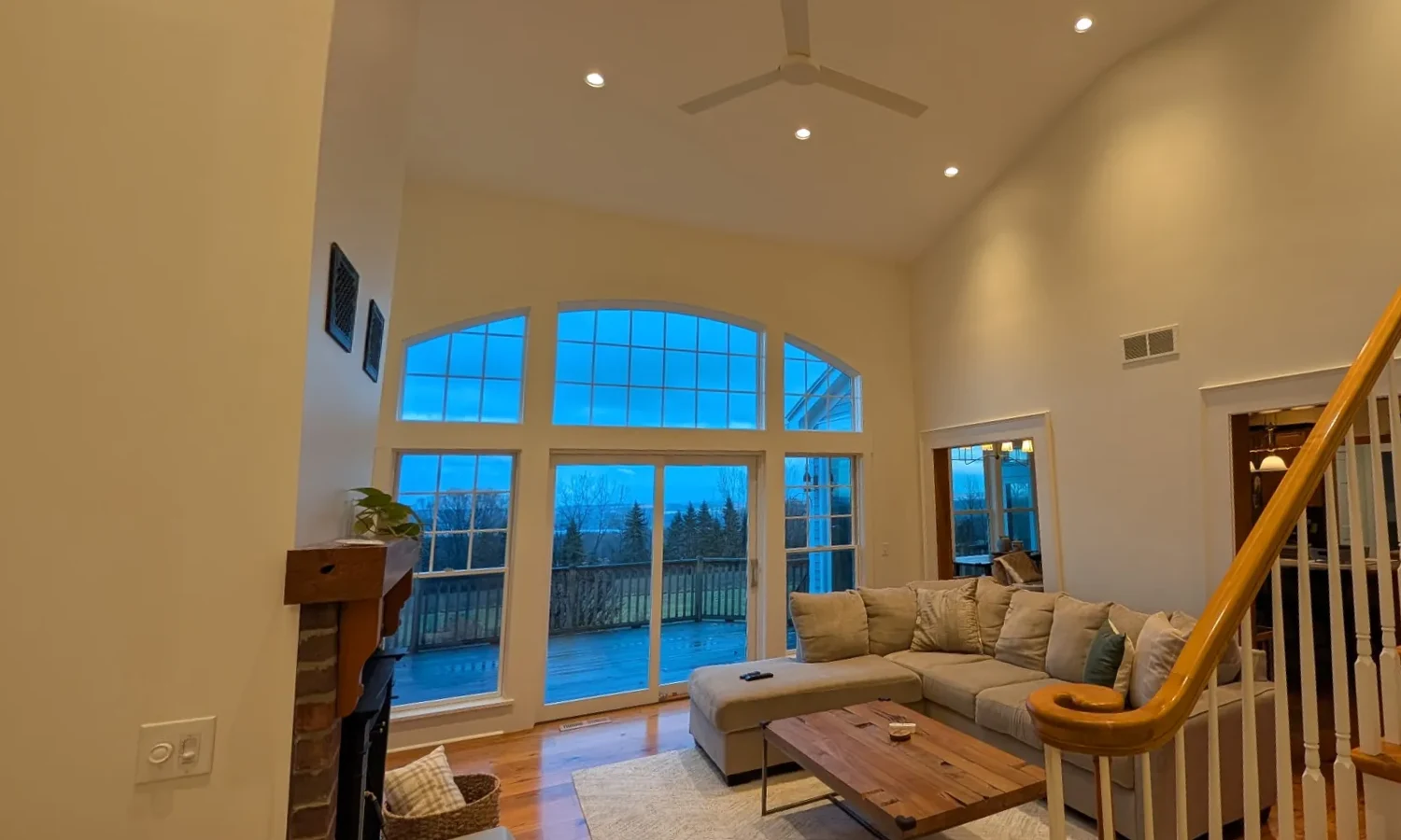 Vaulted living room at dusk with recessed lights, white-trimmed arched windows and a staircase with white balusters
