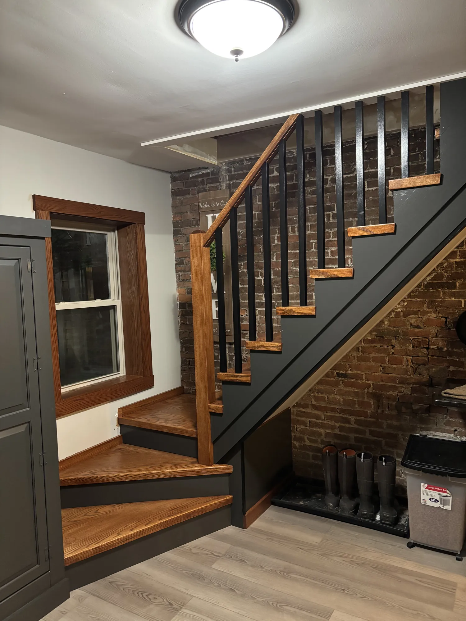 Staircase with stained oak treads, charcoal risers and stringer, black square balusters and oak handrail by exposed brick
