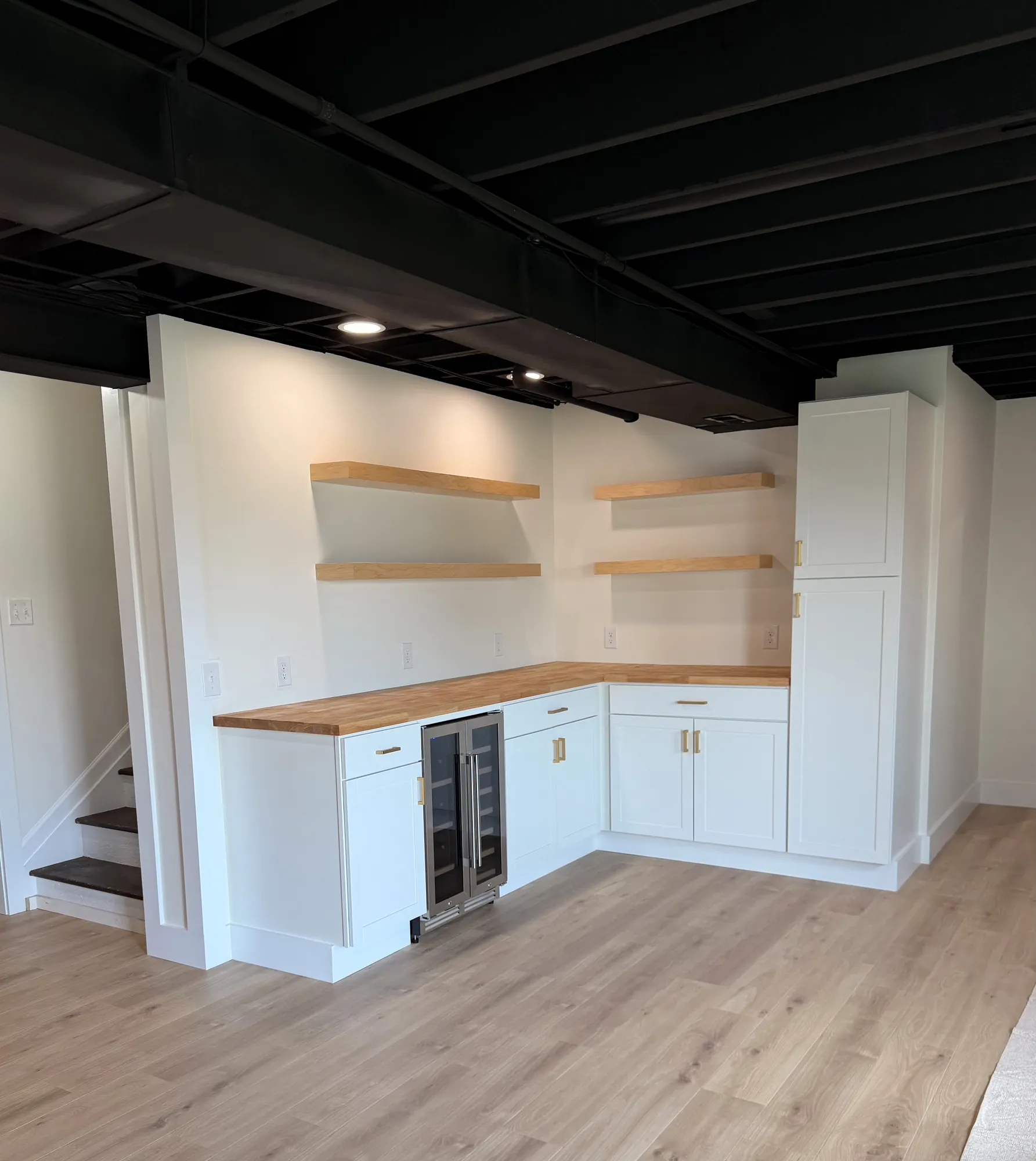 L-shaped wet bar with white shaker cabinets, brass pulls, butcher-block counter, floating wood shelves and a beverage fridge