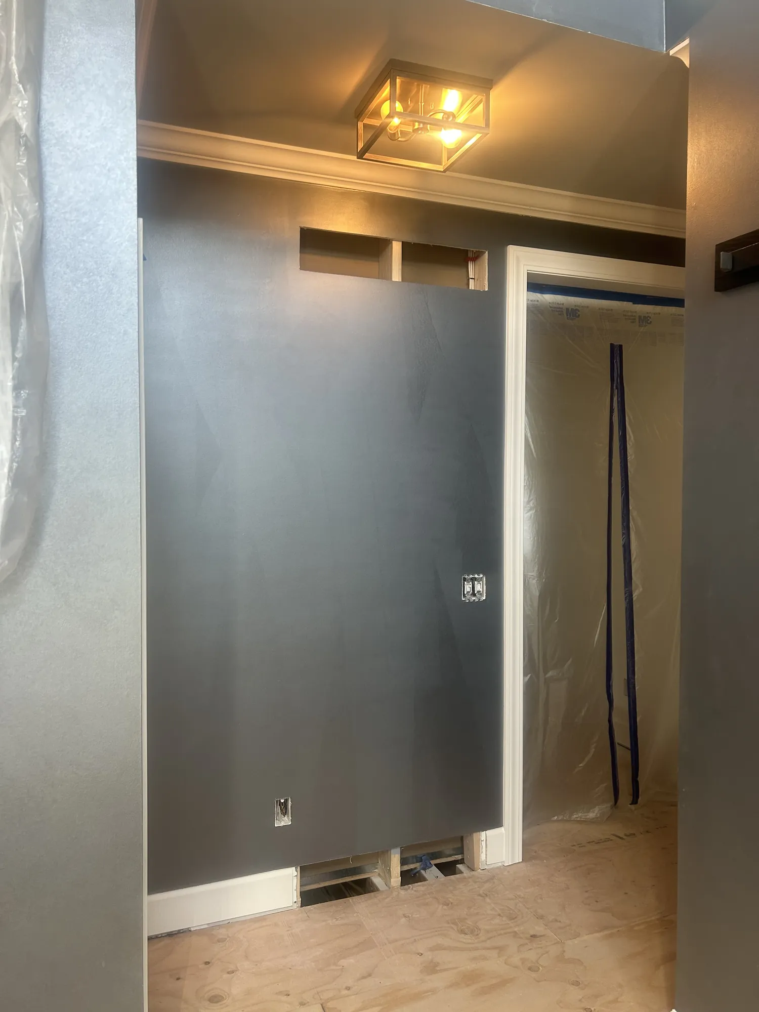Hallway with gray metallic walls under a glass lantern light, white crown and door casing, and a plastic-covered doorway.