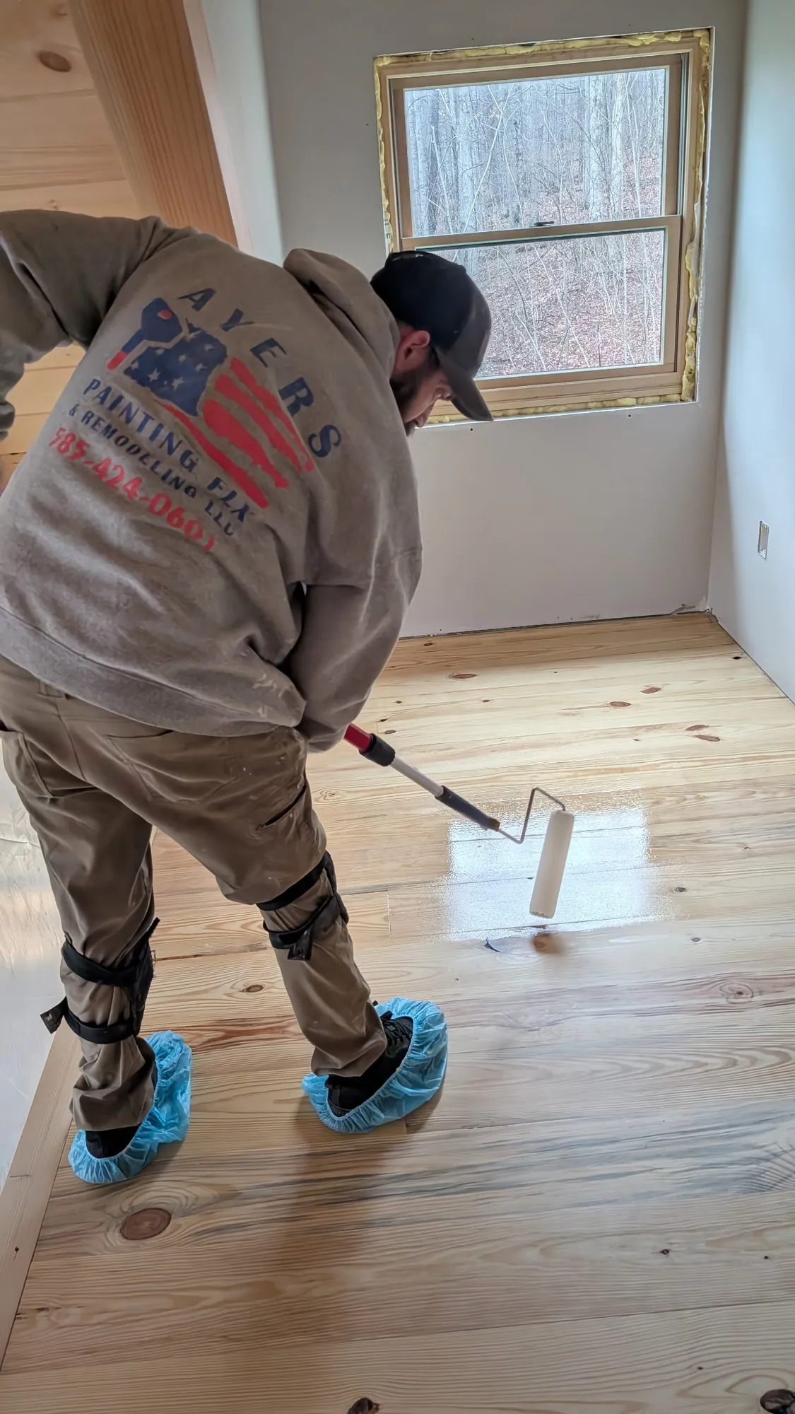 Ayers crew member on his knees, wet clear finish shining on knotty pine boards by a window
