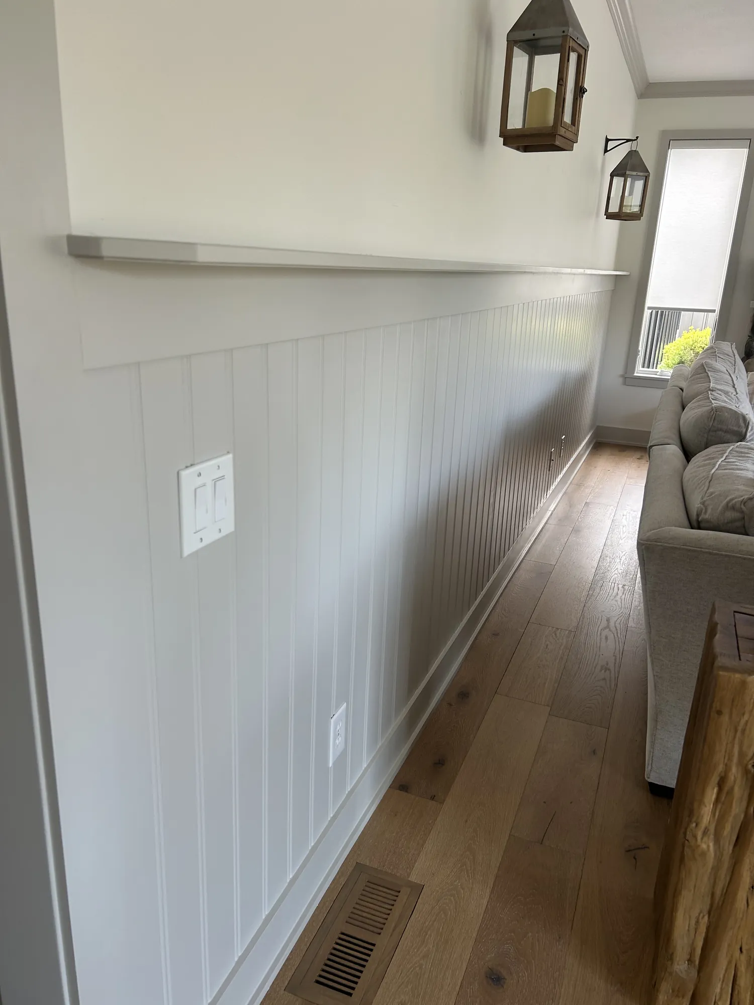 Light gray beadboard wainscoting with a flat ledge cap running the length of a living room wall above a hardwood floor.