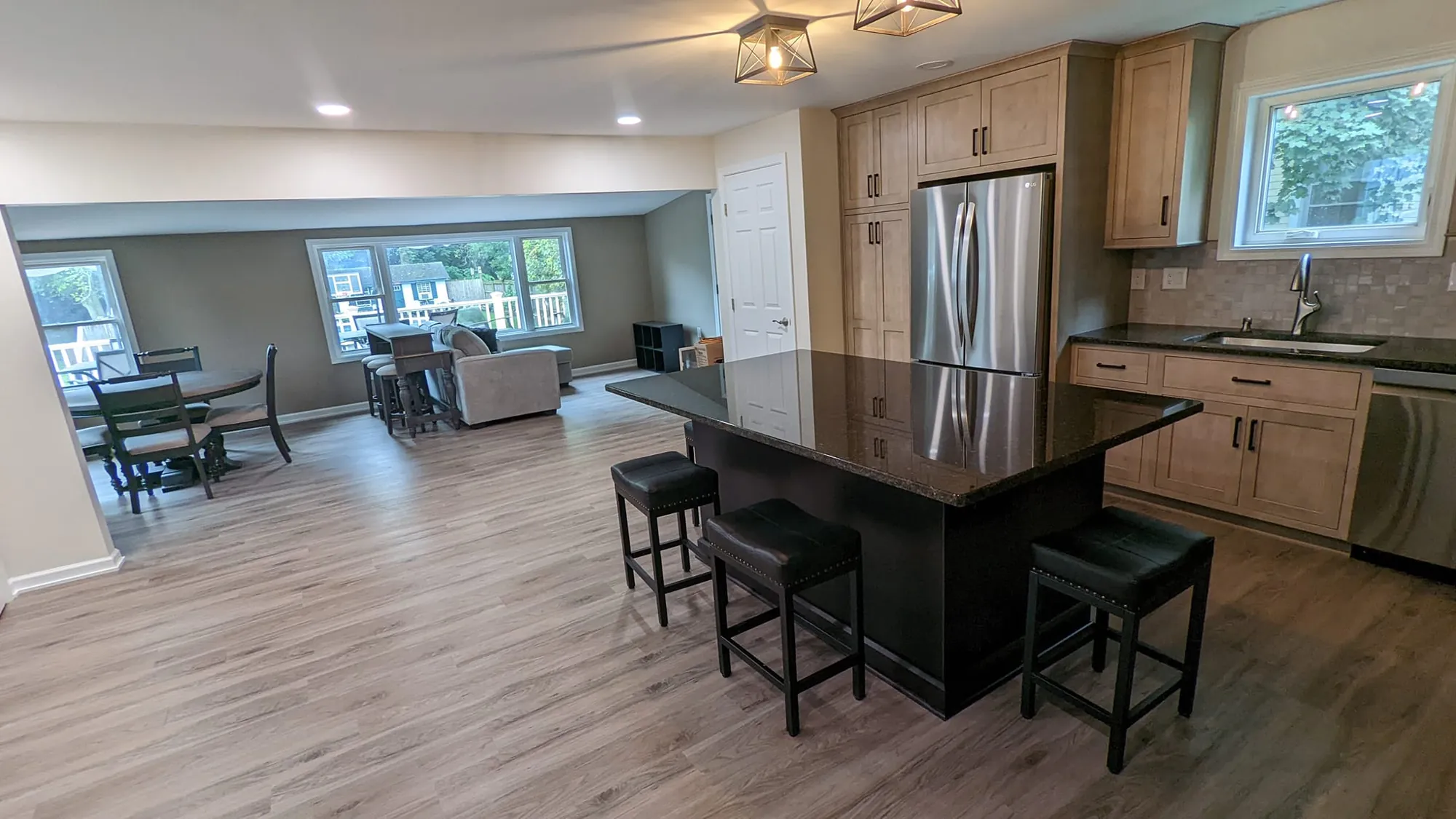 Black kitchen island with three stools and a dark speckled top, open to a dining table and family room with large windows