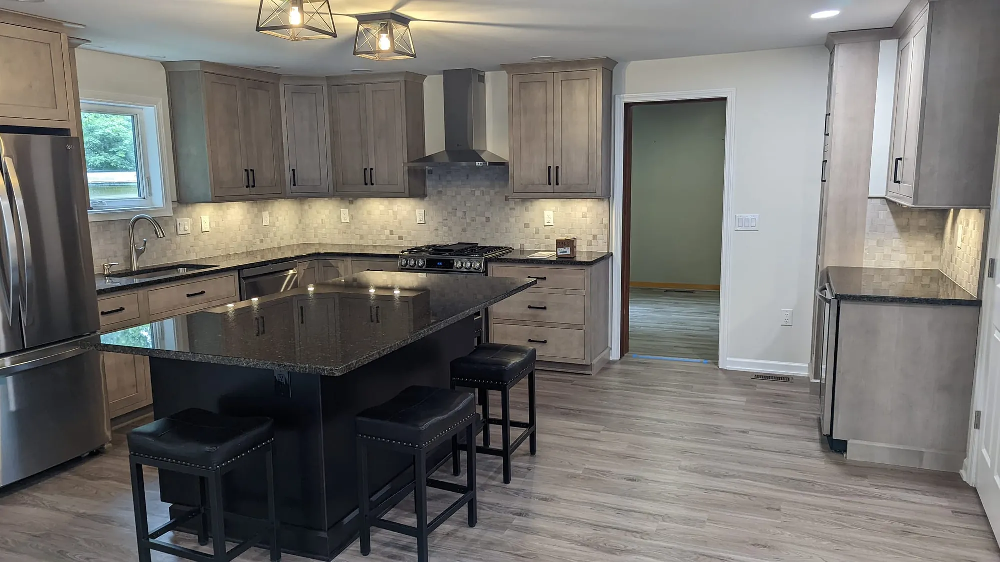 Kitchen with wood-tone shaker cabinets, black island with a dark speckled top and three stools, and a mosaic tile backsplash