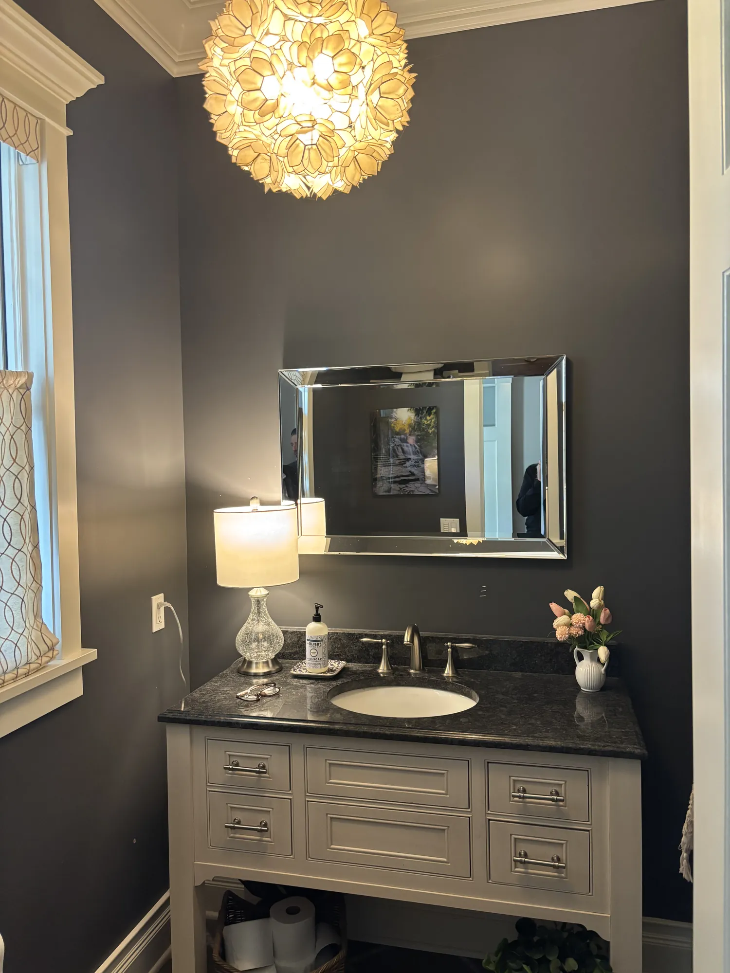 Before: Powder room vanity wall with charcoal walls, white crown molding, a petal pendant light, a framed mirror and a white vanity