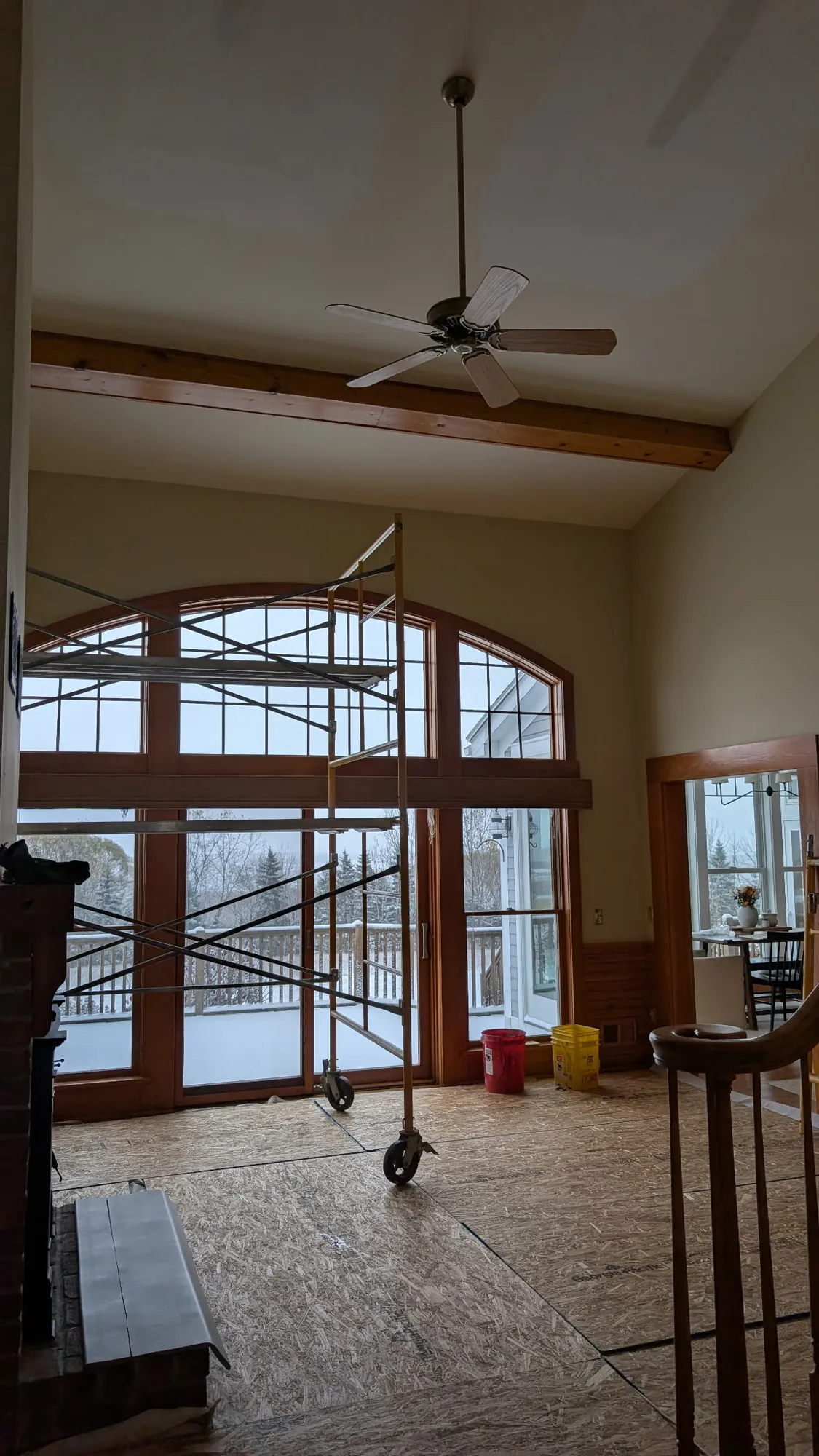 Before: Tall arched windows with stained wood trim under an exposed beam, a rolling scaffold in front and snow outside